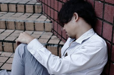 Tired overworked Asian business man sitting outdoors.