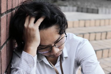 Depresyonda olan, elleri alnında, çok çalışan Asyalı genç bir iş adamı.