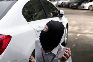 Maskeli tutan küçük taş hazır araba arka plan karşı hırsızlık için bir yün giyen hırsız. Sigorta suç kavramı.