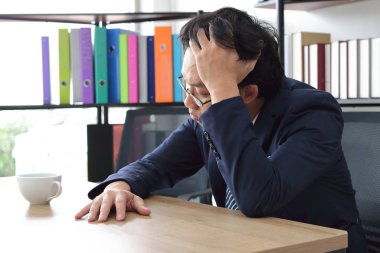Stressed tired young Asian business man with hands on face feeling depression in workplace of office.