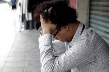 Bastırılmış Asyalı işi, elleri başının üstünde, kaldırımda oturuyor..