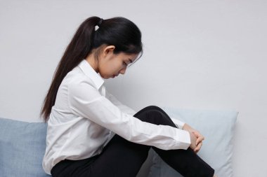 Oturma odasında oturan yorgun ve üzgün Asyalı genç kadının yan görüntüsü.