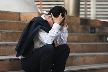 Stresli, takım elbiseli, elleri merdivenlerde oturan Asyalı genç bir iş adamı. İşsizlik ve işten çıkarma kavramı.