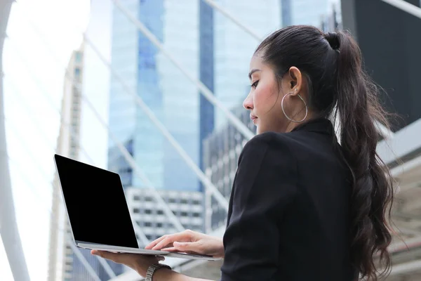 ラップトップ近代的な高層ビルの背景で働くアジアの若いビジネス女性のリーダーシップ — ストック写真