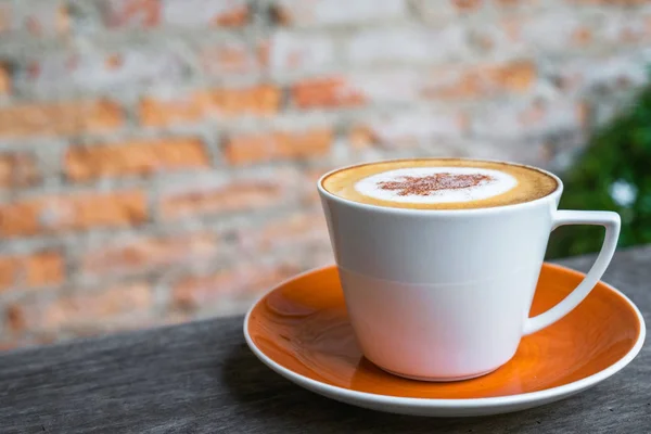 Cappuccino café em copo branco na mesa de madeira com tijolo velho wa — Fotografia de Stock