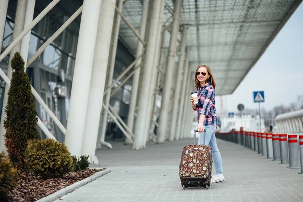 Air travel concept with young hipster businesswoman in plaid shirt with suitcase and disposable cup with coffe or tea. Freedom Travel and Holiday Concept. — Stock Photo, Image