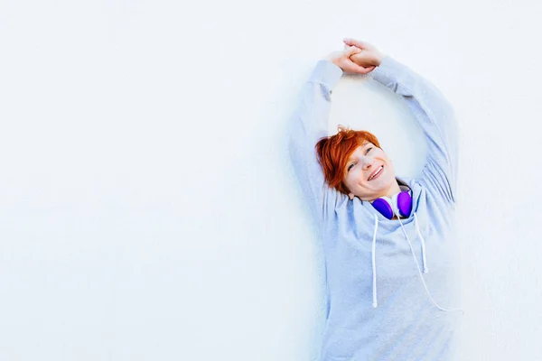 Jeune femme sportive aux cheveux courts rouges qui s'étire contre un mur blanc avant de courir ou d'autres séances d'entraînement. Motivation, sport et santé concept de vie . — Photo