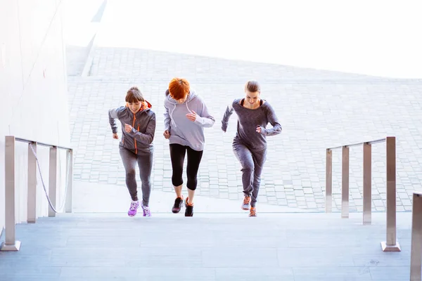 Vista frontal do grupo de três mulheres atléticas correndo escadas acima durante o treinamento cardio-intervalado . — Fotografia de Stock