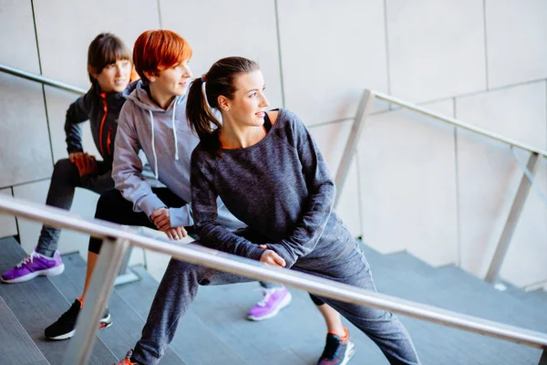 Grupo de tres mujeres deportivas estirándose en las escaleras antes de correr . — Foto de Stock