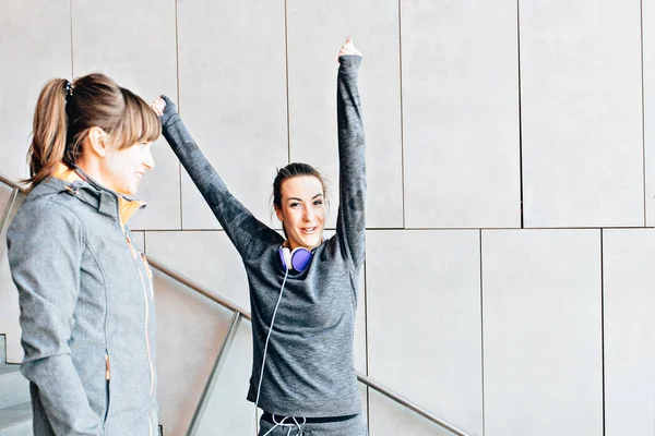 Dos mujeres deportivas en ropa deportiva gris con las manos arriba antes del entrenamiento en las escaleras . — Foto de Stock