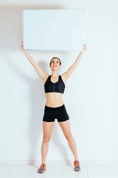 Sonriente fitness mujer sosteniendo hasta vacío tablero por encima de su cabeza, longitud completa, fondo blanco — Foto de Stock