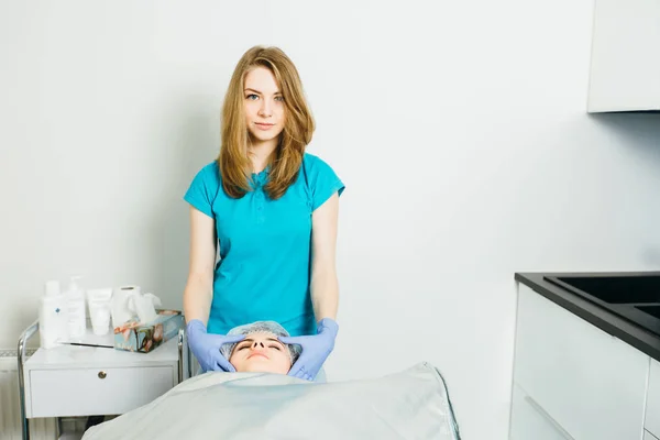 Kosmetikerin im türkisfarbenen T-Shirt bei einer Gesichtsmassage im Wellness-Salon. das Verfahren der Gesichtsmassage im Schönheitssalon. Gesichtspflege. Kosmetologie. Kosmetikerin macht Massage für Klient — Stockfoto