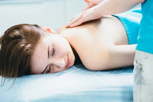 Close-up van de jonge vrouw liggend vestured turquoise handdoek terwijl massagetherapeut masseren van haar schouders. Beauty, gezondheid leven en cosmetologie concept. — Stockfoto