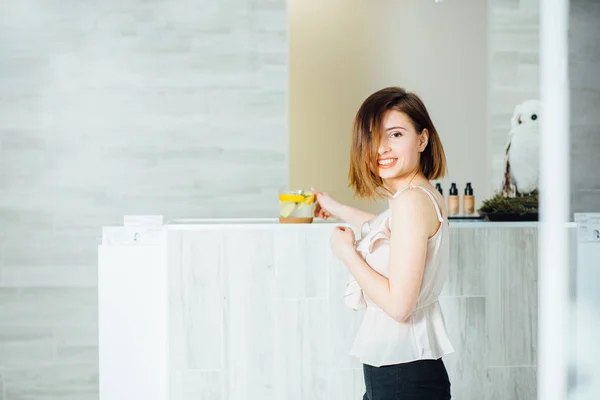 Bienestar, salud, estilo de vida. Joven mujer gorgeos oliendo con pelo castaño corto esperando delante de la recepción en salón de belleza o spe . — Foto de Stock