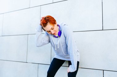 Duvara karşı yaslanmış kısa Kızıl saçlı genç sportif erkek içinde Hoody giyiyor. Genç hipster kadın koşu sonra rahatlatıcı. Sağlıklı yaşam ve spor kavramları