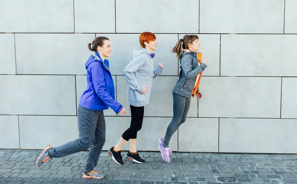 Três corredores sprint ao ar livre - Treinamento mulher esportiva sobre a parede urbana, vista lateral. Estilo de vida saudável e conceitos desportivos — Fotografia de Stock