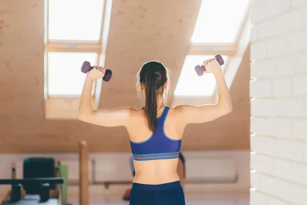 Mujer haciendo ejercicio con pesas en un gimnasio. Vista trasera . — Foto de Stock