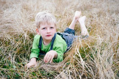 Küçük çocuk kot ve Yeşil tişörtlü çimenlerin üzerinde oturuyor. Çocukluk tatil kavramı