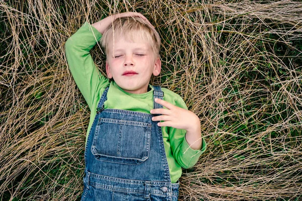 Top view of little 5 years old boy in blue jeans and green shirt lying on grass. Childhood vacations concept — Stock Photo, Image