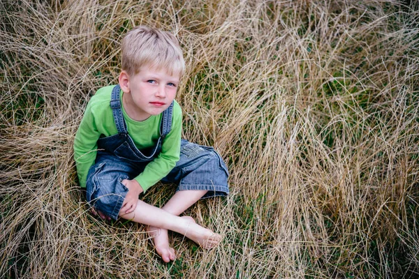 Little boy in blue jeans and green shirt sitting on the grass. Childhood vacations concept — Stock Photo, Image