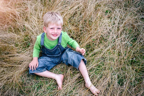 Jongetje in spijkerbroek en groene shirt zittend op het gras. Jeugd vakanties concept — Stockfoto