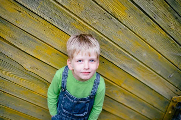 Эмоциональный портрет маленького мальчика в зелёной футболке, играющего перед жёлтым деревенским деревянным забором. Серия фото — стоковое фото