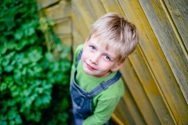 Retrato emotivo de un niño pequeño con una camiseta verde jugando frente a la cerca de madera rústica amarilla. Foto de serie —  Fotos de Stock
