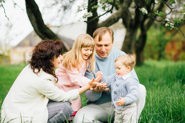 Gelukkig gezin met twee kinderen met plezier in de apple-tuin en spelen met bloemen van apple blossom in hun handen op een lentedag. — Stockfoto