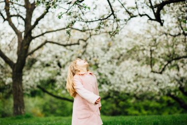 Elma Bahçe bahar zaman döne döne çocuk. Sevimli küçük kız bahar çiçek açması bahçede oynayan gül ceket giymiş
