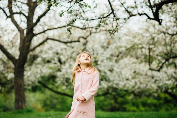 Chico girando en el jardín de manzanas en primavera. Linda niña vestida con abrigo de rosa jugando en el jardín de flores de primavera —  Fotos de Stock