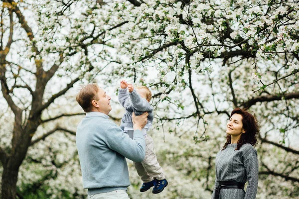 Familia petrece timp împreună în parc în timpul primăverii. Mama se uită la fiul cel mic și-l trece la tatăl său . — Fotografie, imagine de stoc