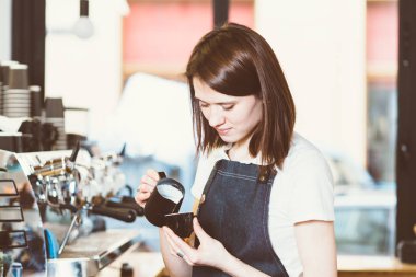 Kahve için süt ekleyerek ve barda duran gülümseyen genç kadın barista kentsel Cafe counter