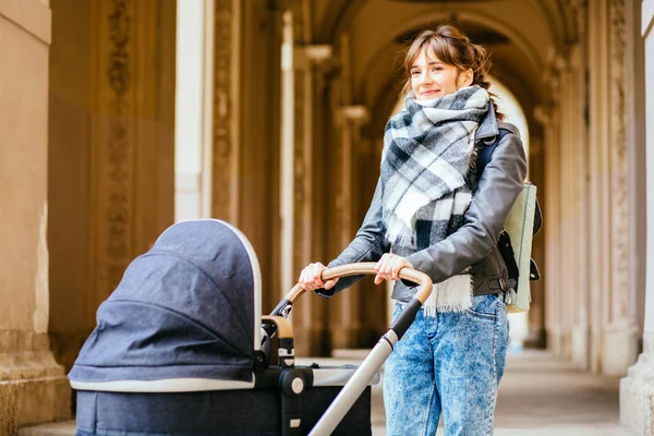 Madre morena de moda en una calle de la ciudad con un cochecito. Madre joven camina con un niño en la ciudad. Hermosa mujer joven con un niño en un carro de bebé — Foto de Stock