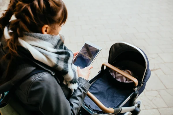 Vista superior de la tenue madre morena con cochecito de bebé haciendo foto por tableta Madre joven camina con un niño en la ciudad. Hermosa mujer joven con un niño en un carro de bebé — Foto de Stock