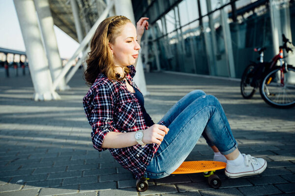 Pretty teen girl sitting and rolling on skateboard