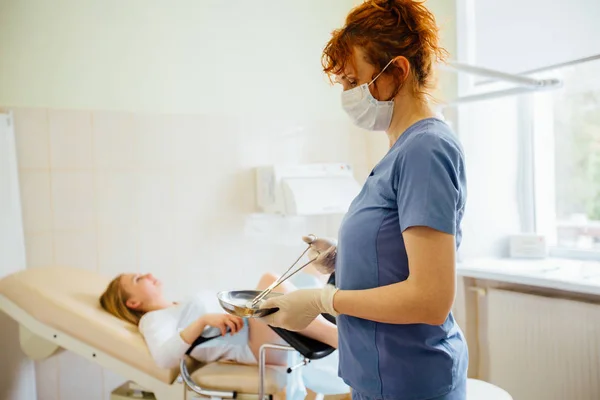 Cheveux roux femme médecin tenant outil dans un bassin en acier devant la patiente sur chaise gynécologique . — Photo