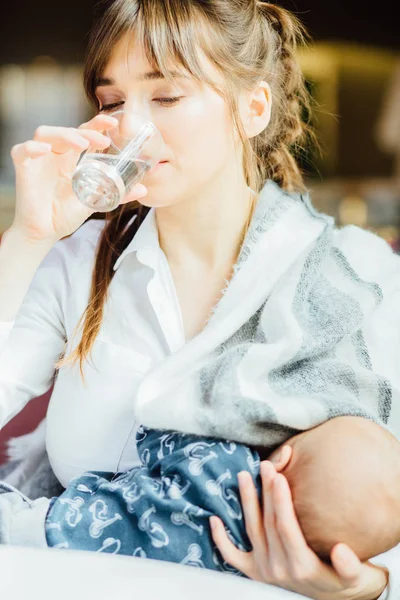 Вертикальный портрет молодой очаровательной матери, пьющей воду во время кормления грудью мальчика — стоковое фото