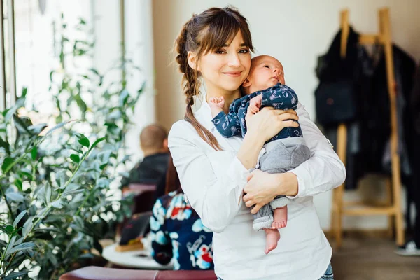 Счастливая очаровательная мать в белой рубашке обнимает и держит своего маленького сына в помещении кафе . — стоковое фото