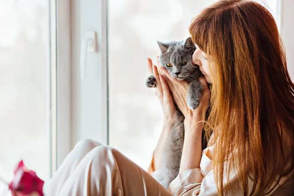 Kedves középkorú vörös hajú nő megcsókolta szürke macska közelről. — Stock Fotó