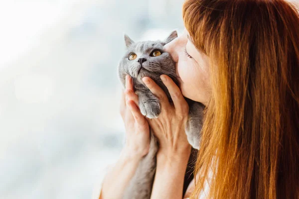 Close up of lovely middle-aged redhead woman kissing gray cat. — Stock Photo, Image