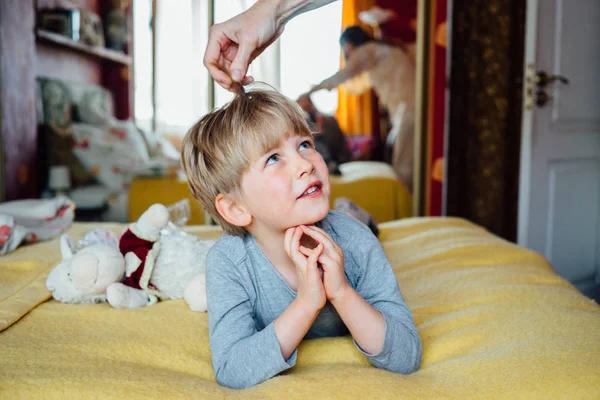 Leuke knappe jongen 5 jaar op het bed liggen en spreken met de moeder. Moederdag hand corrigeert de haren van het kind. — Stockfoto