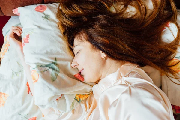 Kızıl saçlı güneşli sabah yatakta uyuyan güzel orta yaşlı kadının Üstten Görünüm.