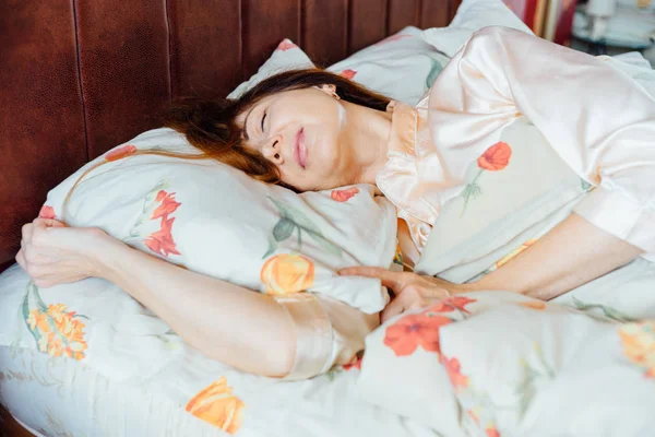 Portrait of charming middle aged woman with red hair sleeping on the bed in sunny morning.