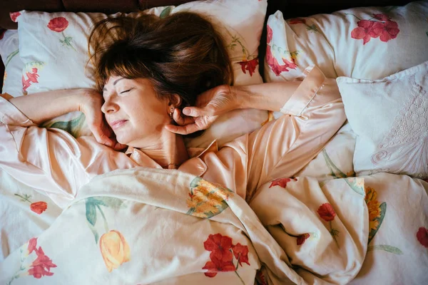 Top view of charming middle aged woman with red brown hair in sleepwear slowly wake up in the bed . — стоковое фото