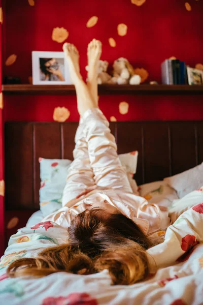 Вертикальный портрет очаровательной молодой женщины в сонной одежде, расслабляющей ноги в постели . — стоковое фото