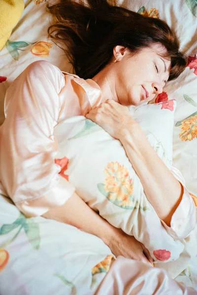 Вид сверху красивой женщины средних лет с рыжими волосами, спящей и обнимающей подушку на кровати солнечным утром . — стоковое фото