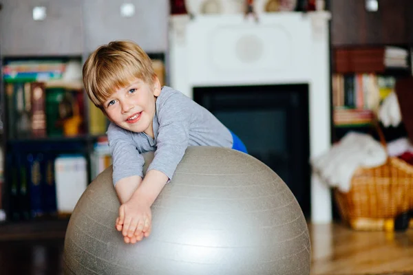 Leuke knappe jongen 5 jaar trainen en spelen met een grote gymnastiek bal thuis. — Stockfoto
