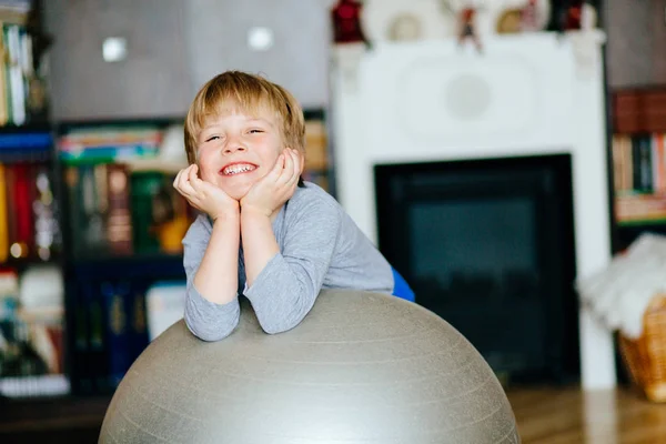 Schattig glimlachend jongen 5 jaar trainen en spelen met een grote gymnastiek bal thuis. — Stockfoto