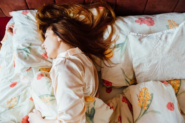 Top view of charming middle aged woman with red brown hair in rose sleepwear slowly sleeping in the bed . — стоковое фото