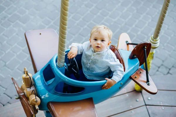 Sarı saçlı ve mavi gözleri kameraya vintage mavi uçak carousel ve göz üzerinde oturarak yürümeye başlayan çocuk — Stok fotoğraf